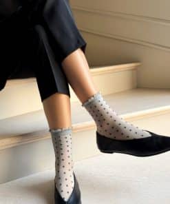 Person sitting on stairs with sheer polka dot socks and black flats, showing stylish legwear detail.