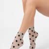 Woman’s legs crossed wearing sheer beige ankle socks with large black polka dots against a white background.