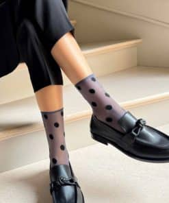 Person sitting on stairs wearing sheer polka-dot socks and black loafers on a light staircase step-by-step scene designer vibe