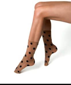 Legs in tan sheer dotted tights with black polka dots, crossed over each other against a white background (Visone brand shown).