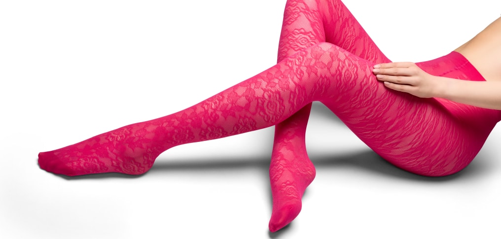 Person wearing bright pink lace tights with legs crossed on a white background.