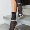 Close-up of legs in black patterned sheer socks with white strappy high heels stepping on concrete stairs.